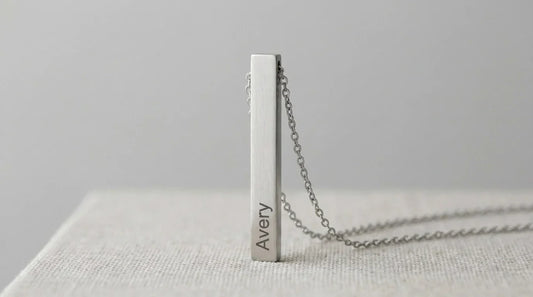 Silver vertical bar necklace pendant engraved with name Avery on fabric surface