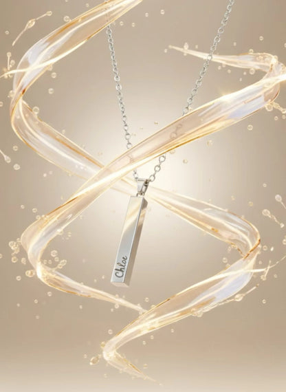 Silver bar pendant necklace with engraving surrounded by swirling golden liquid on beige background
