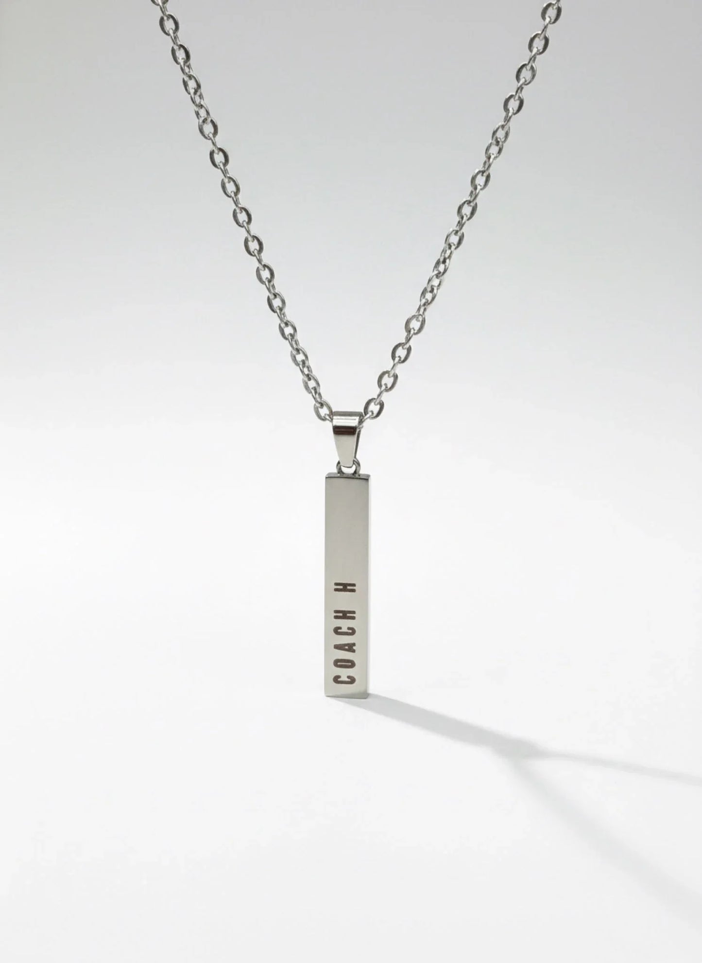 Silver bar pendant necklace with COACH logo on a silver chain against white background