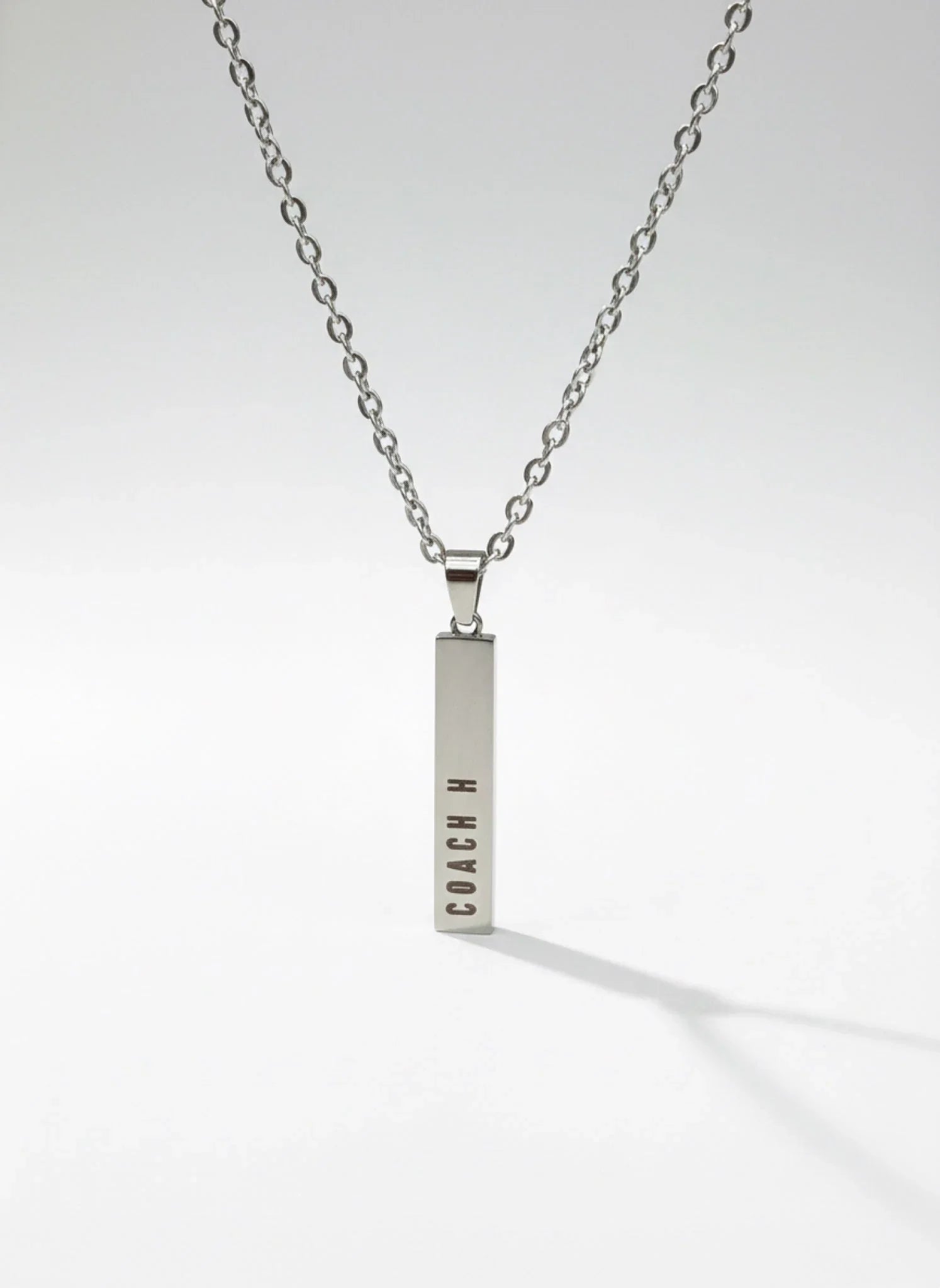 Silver bar pendant necklace with COACH logo on a silver chain against white background