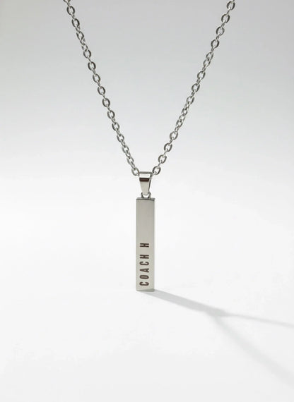 Silver bar pendant necklace with COACH logo on a silver chain against white background