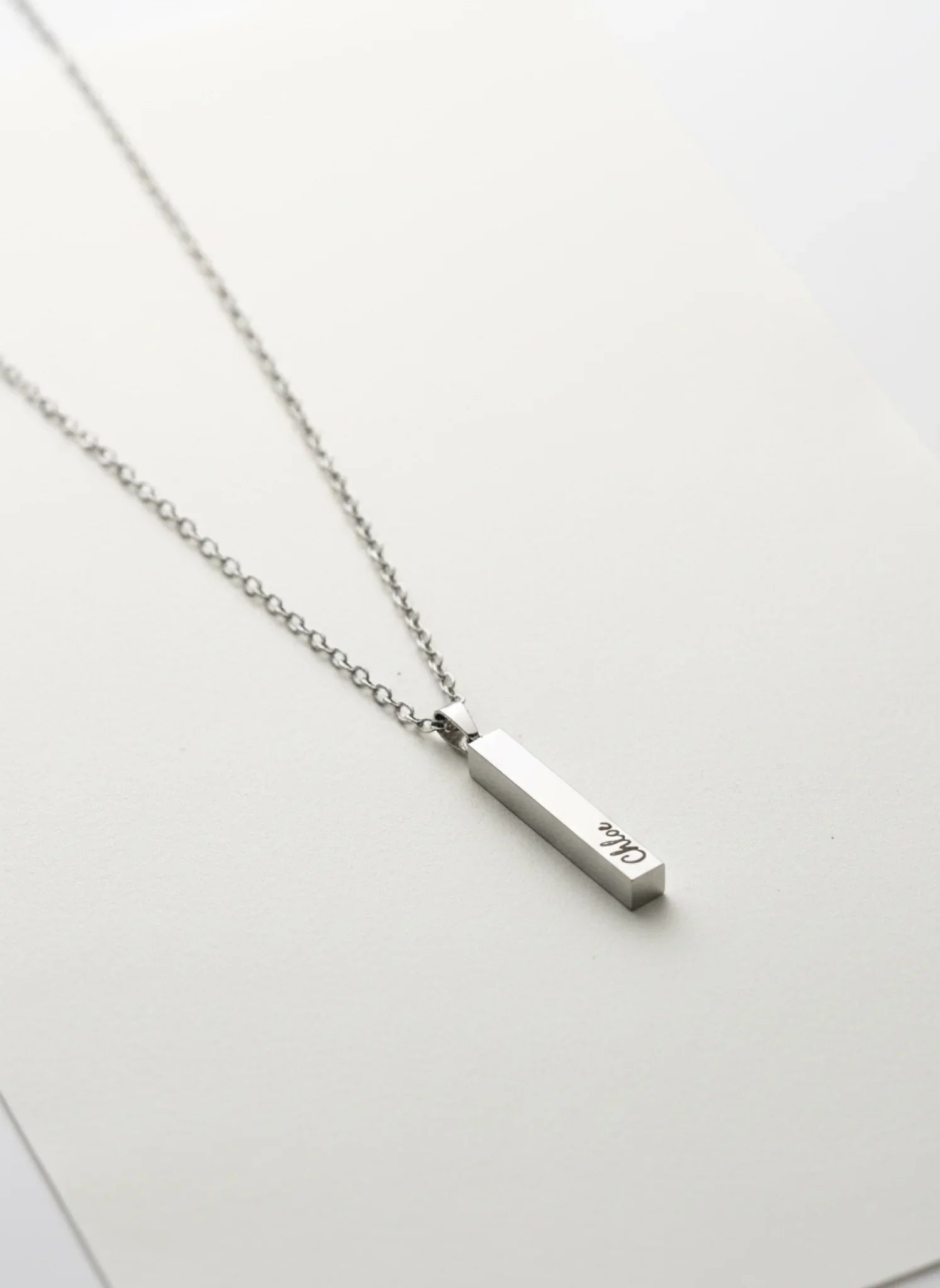 silver vertical bar pendant necklace with engraved name on silver chain on white background
