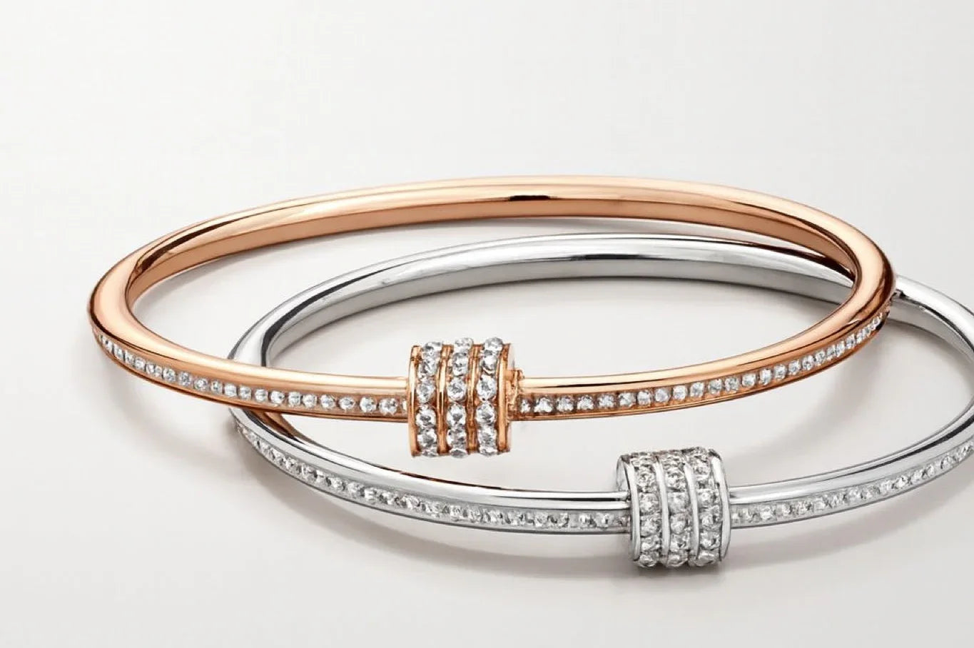 Two elegant diamond-studded bangles, one rose gold and one silver, on white background